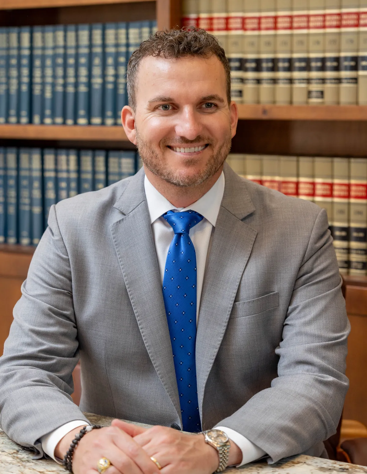 Kellen Bradley smiling at a granite table in front of shelves of law books, in a gray suit and blue tie.