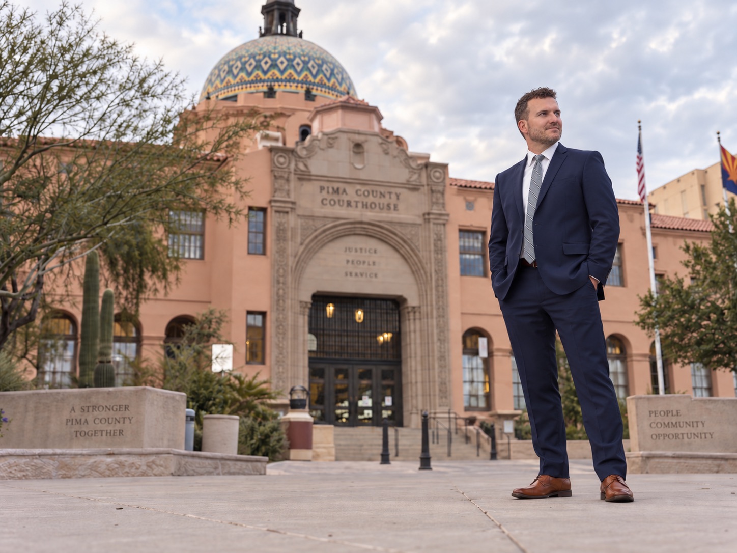 Kellen Bradley standing outside the Pima County Courthouse in Tucson, the tiled dome and pink adobe facade behind him.
